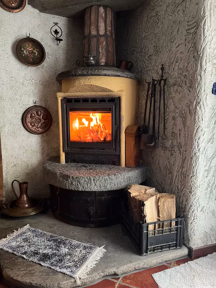 Traditional wood-burning fireplace with glowing fire, stone surround and logs in basket